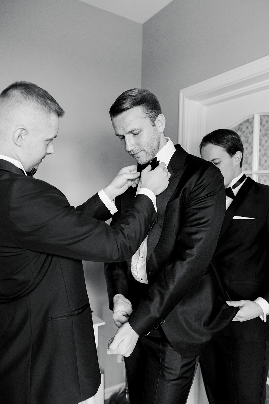 A series of black and white photos showing groomsmen helping each other prepare in formal attire.