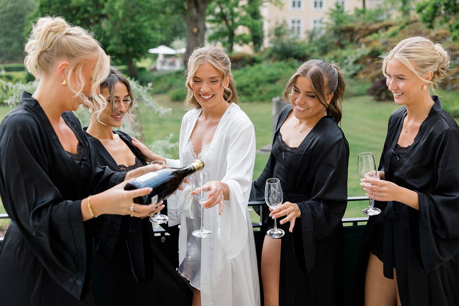 Wedding party members in black and white attire share champagne and laughter during outdoor celebration.
