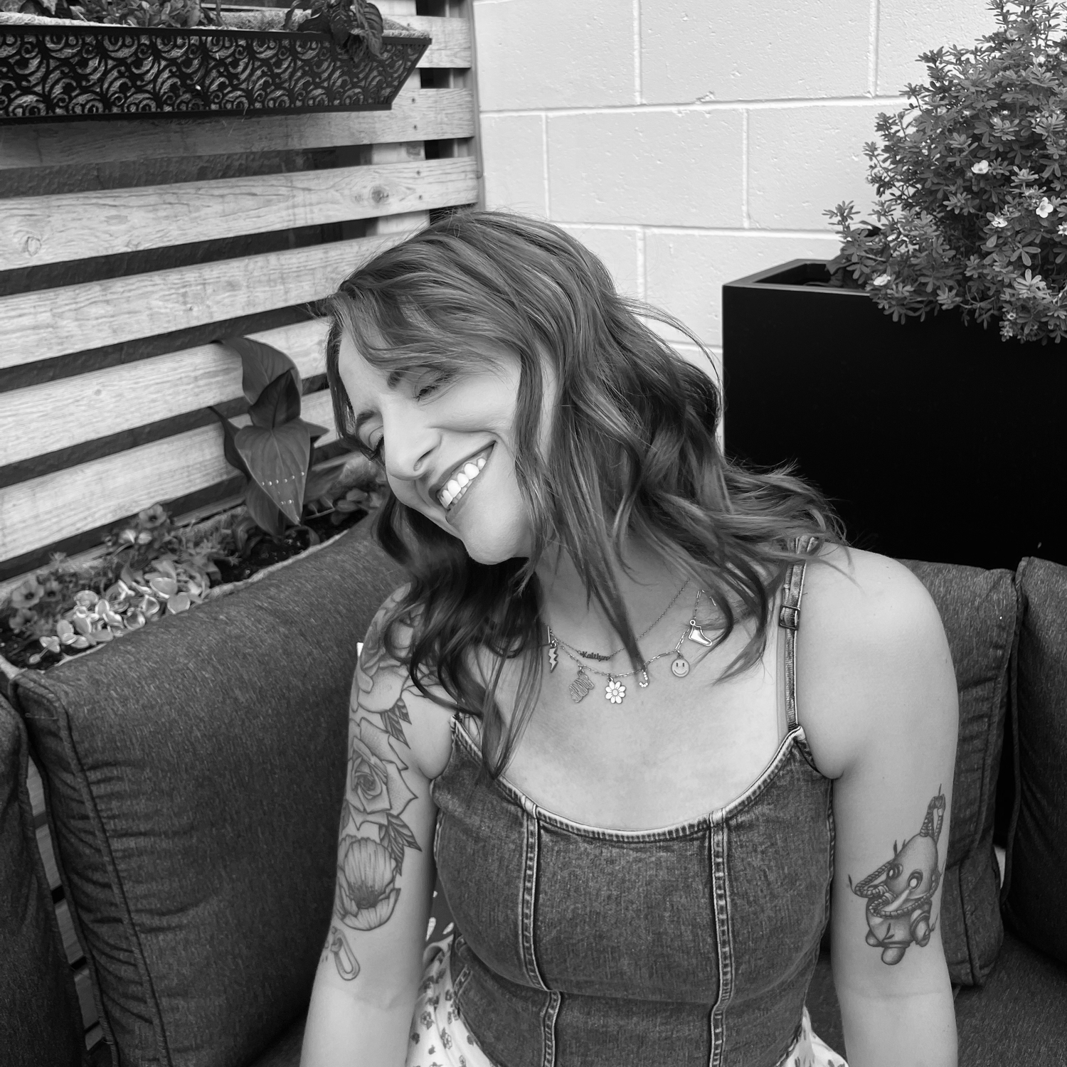 A candid black and white portrait of someone with tattoos relaxing on outdoor furniture.