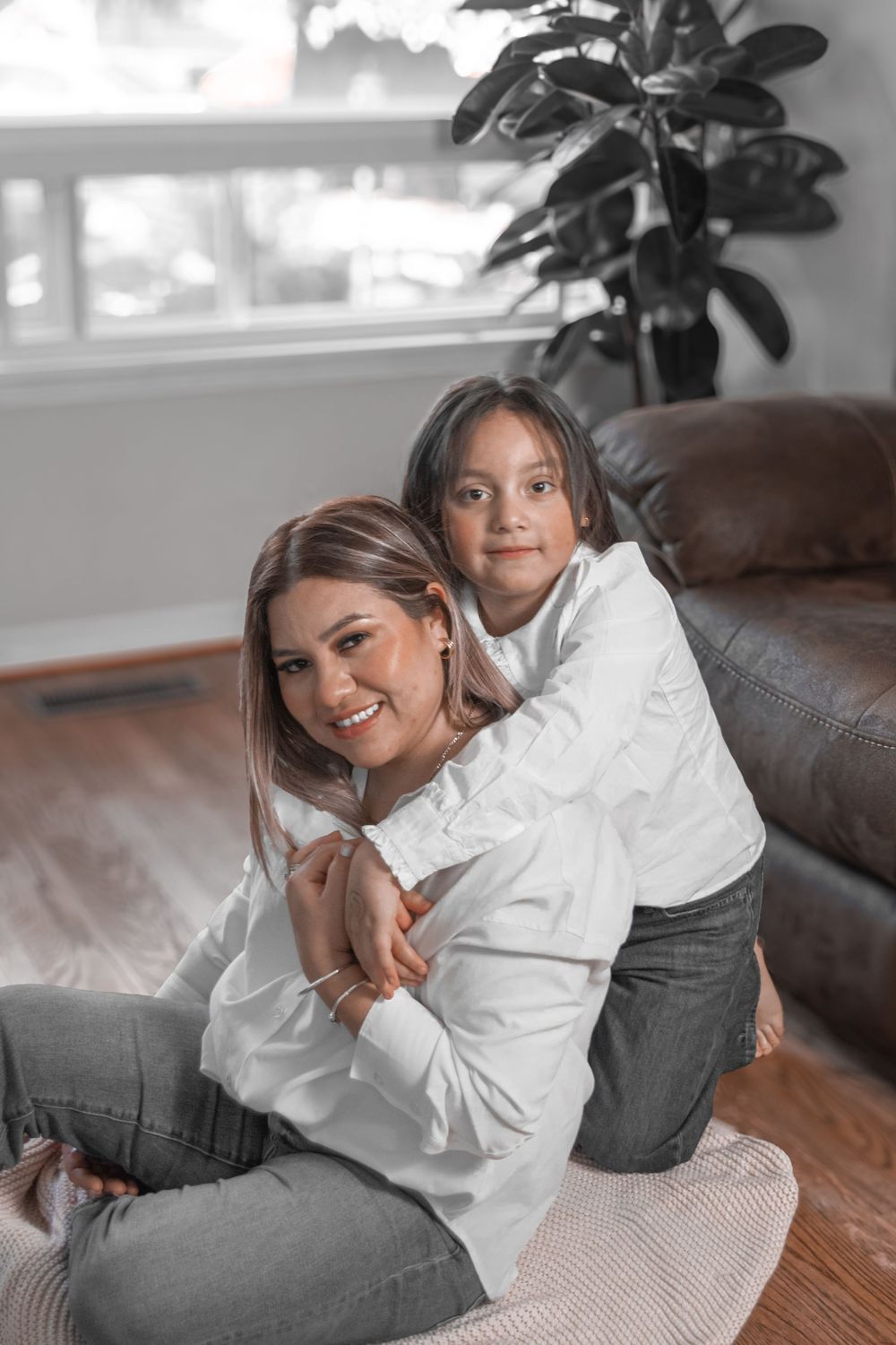 A person in a white blouse and gray pants lounges casually on a brown leather couch in a bright room.