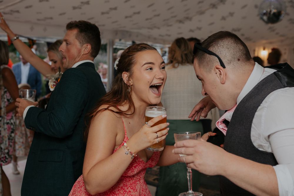 Laughing wedding guest holds a pint of beer while celebrating at a lively wedding reception party.