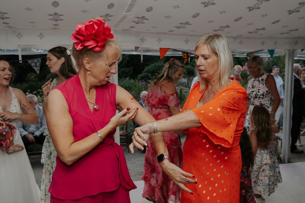 Two women in bright pink and orange dresses dance together at a festive wedding reception.
