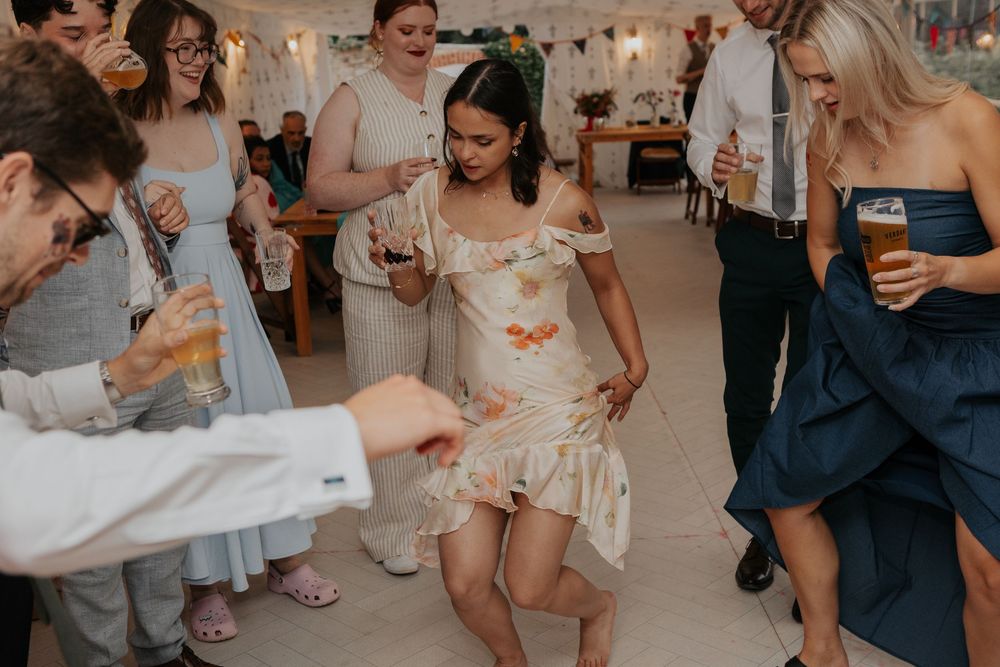 Guests dance energetically at a wedding reception, woman in floral dress twirls on the dance floor.