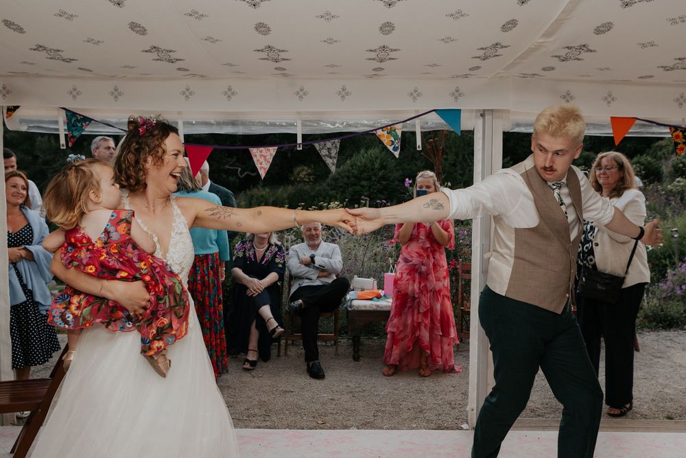 Bride and groom share first dance in a decorated marquee tent with colorful bunting at their wedding.