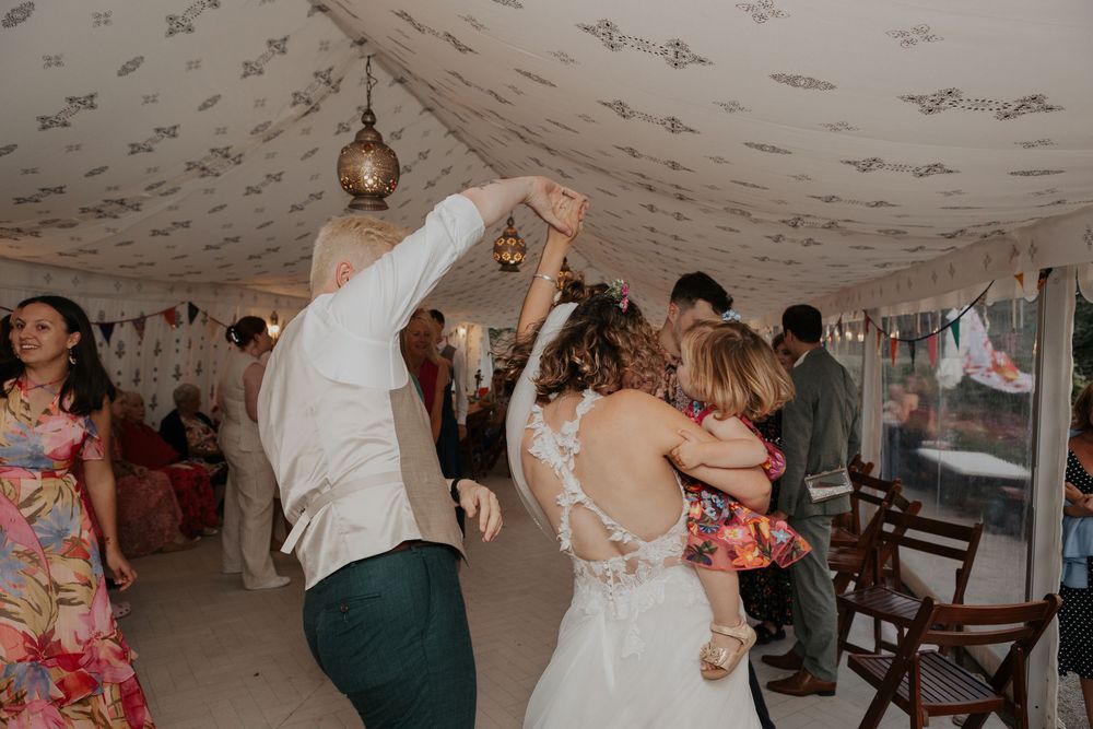 Bride in lace backless gown dances with groom in a beautifully decorated wedding marquee with guests watching.