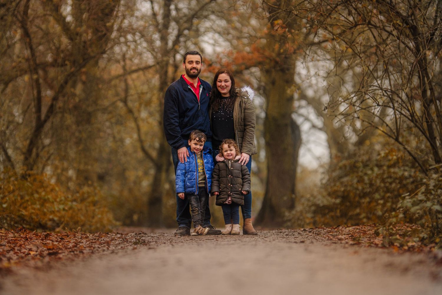 Family stands together on a misty autumn path surrounded by fallen leaves.