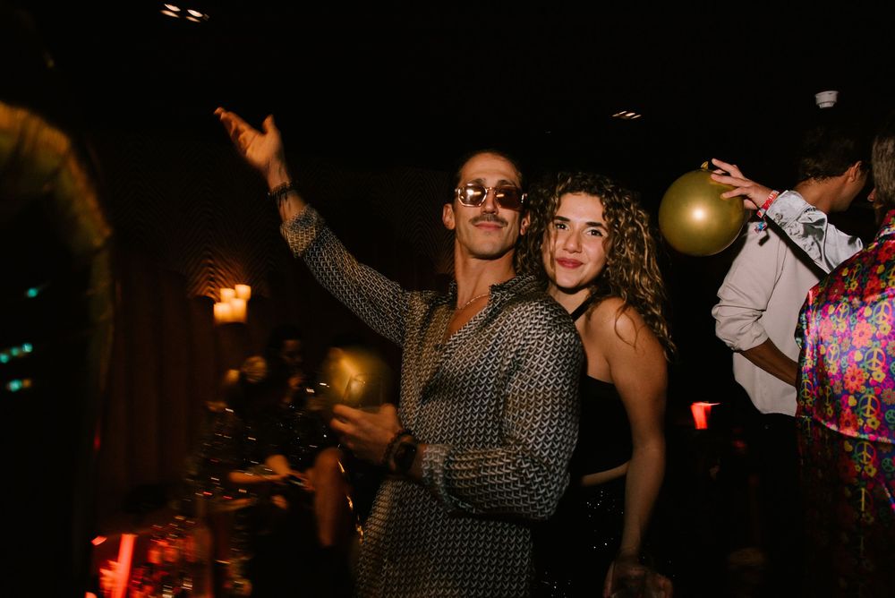 People dancing and celebrating at a lively party with golden balloons in a dimly lit venue.