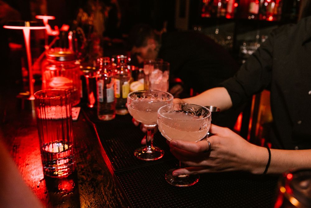 Cocktail glasses illuminated by red ambient lighting in a dark bar setting create a moody atmosphere.