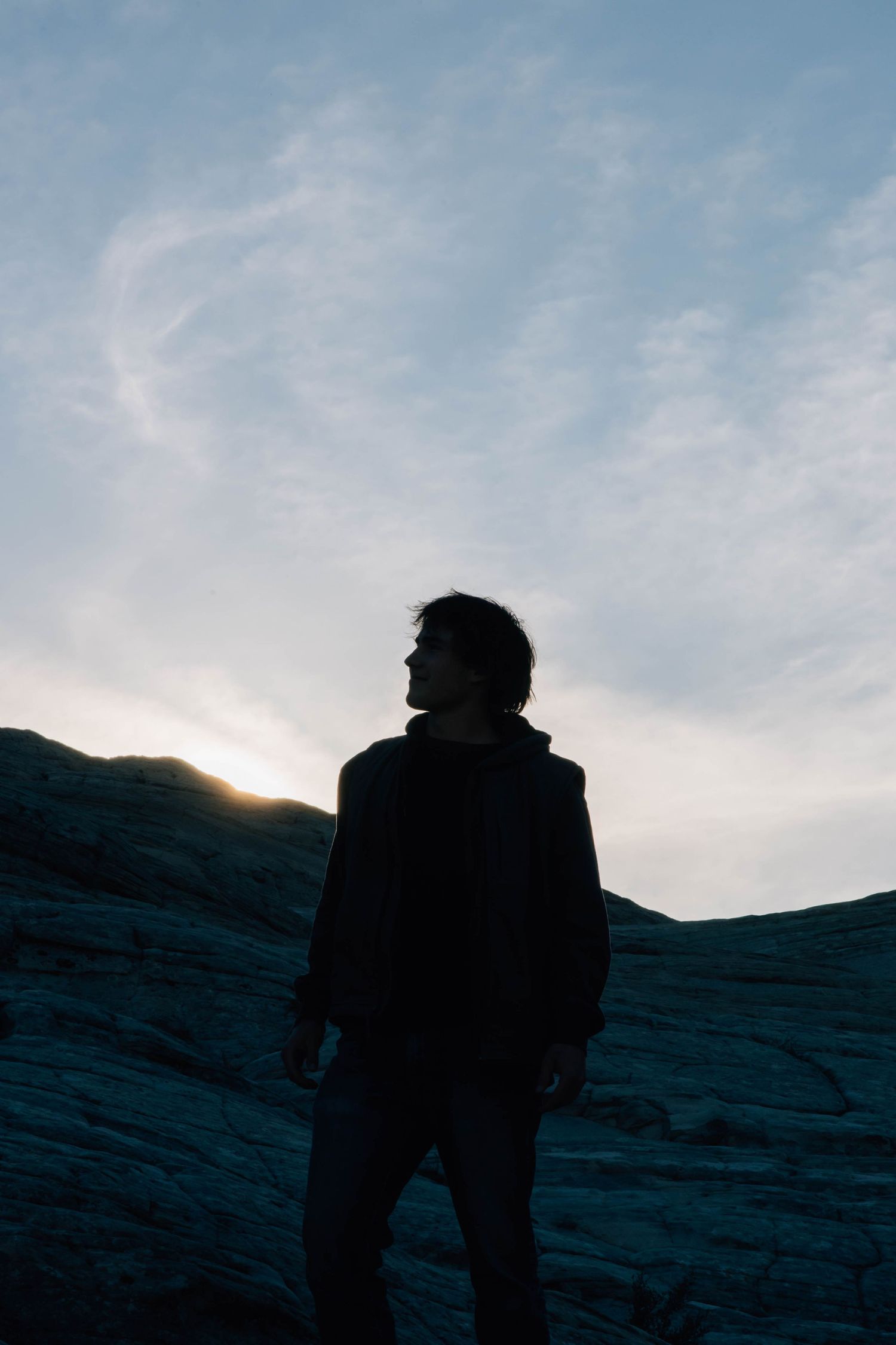Silhouette of young man standing on rocky terrain against dramatic sunset sky.