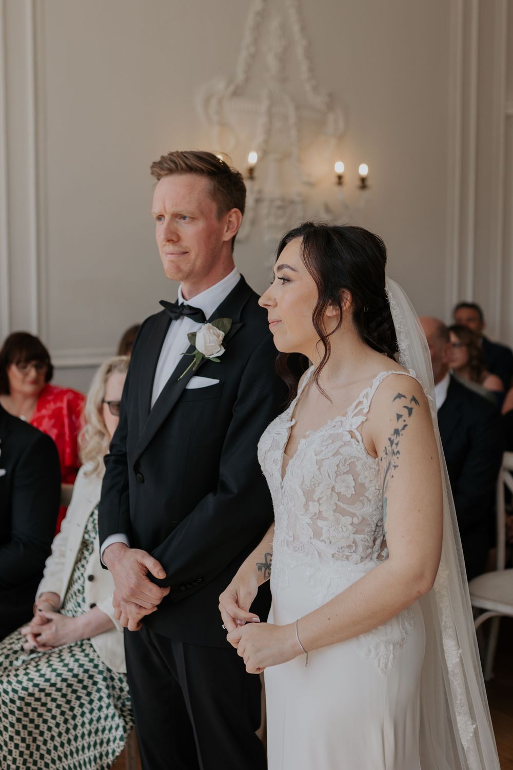 Bride and groom stand together at altar holding hands during elegant indoor wedding ceremony.