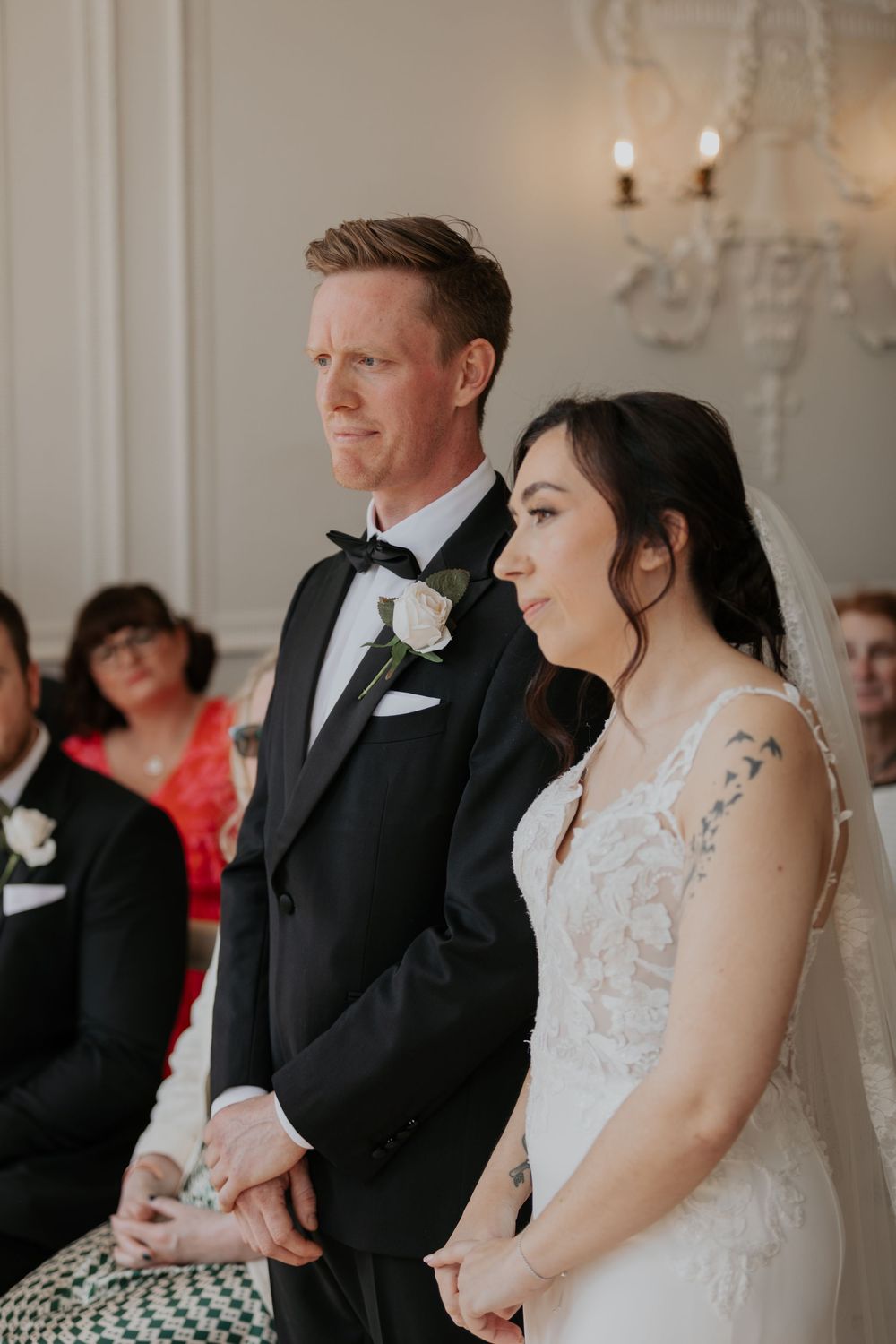 Bride and groom hold hands at altar during romantic indoor wedding ceremony with guests.