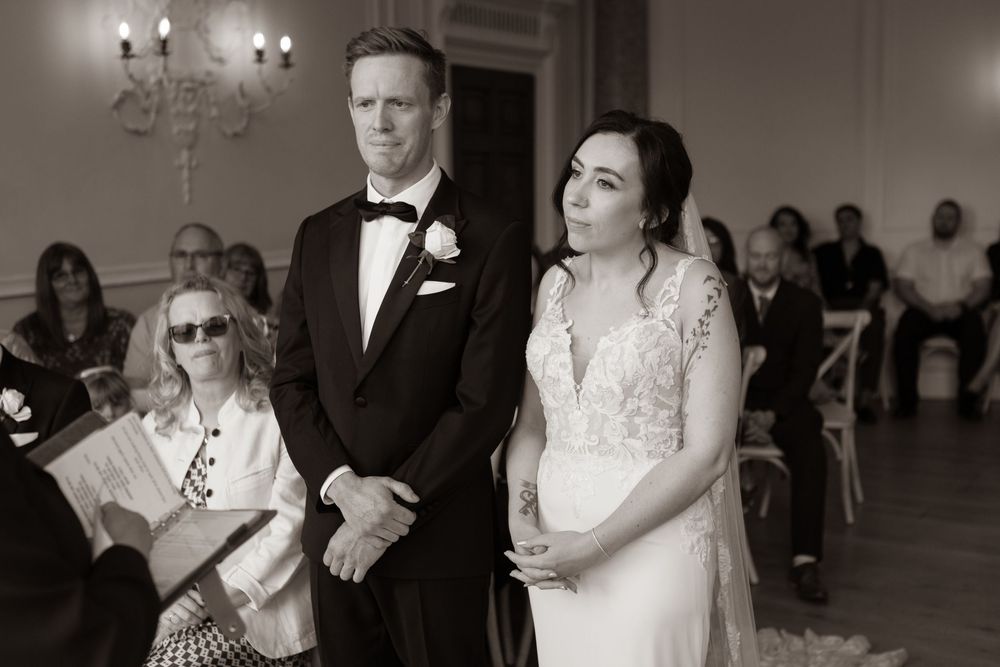 Black and white photo of bride and groom standing at altar with seated wedding guests.