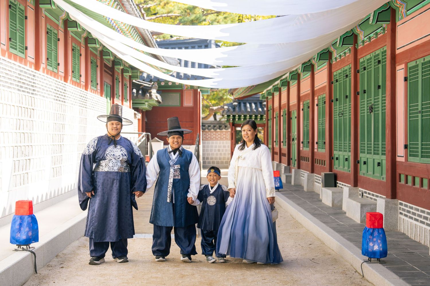 People in traditional Korean hanbok clothing walk through a covered walkway at a historic palace complex.