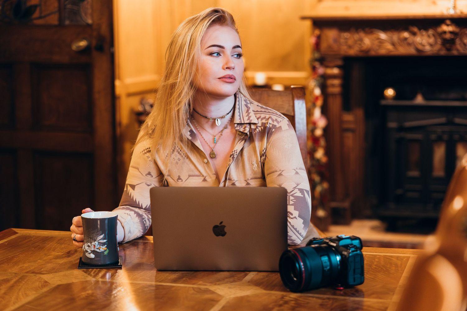 Creative professional working on MacBook laptop with camera and coffee in cozy indoor setting with warm lighting.