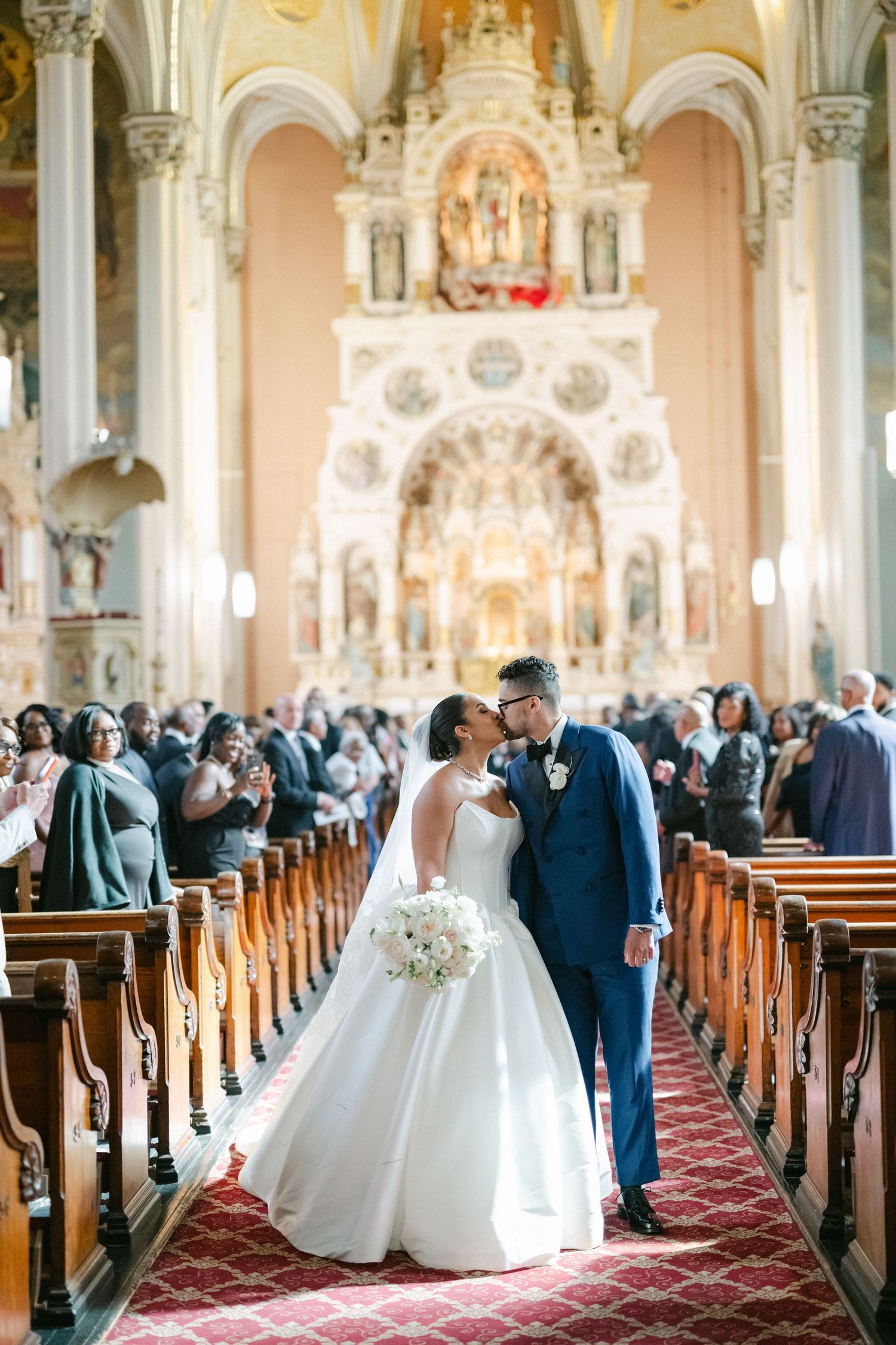 Wedding ceremony in a grand cathedral with ornate architecture, red carpet aisle, and guests filling wooden pews.