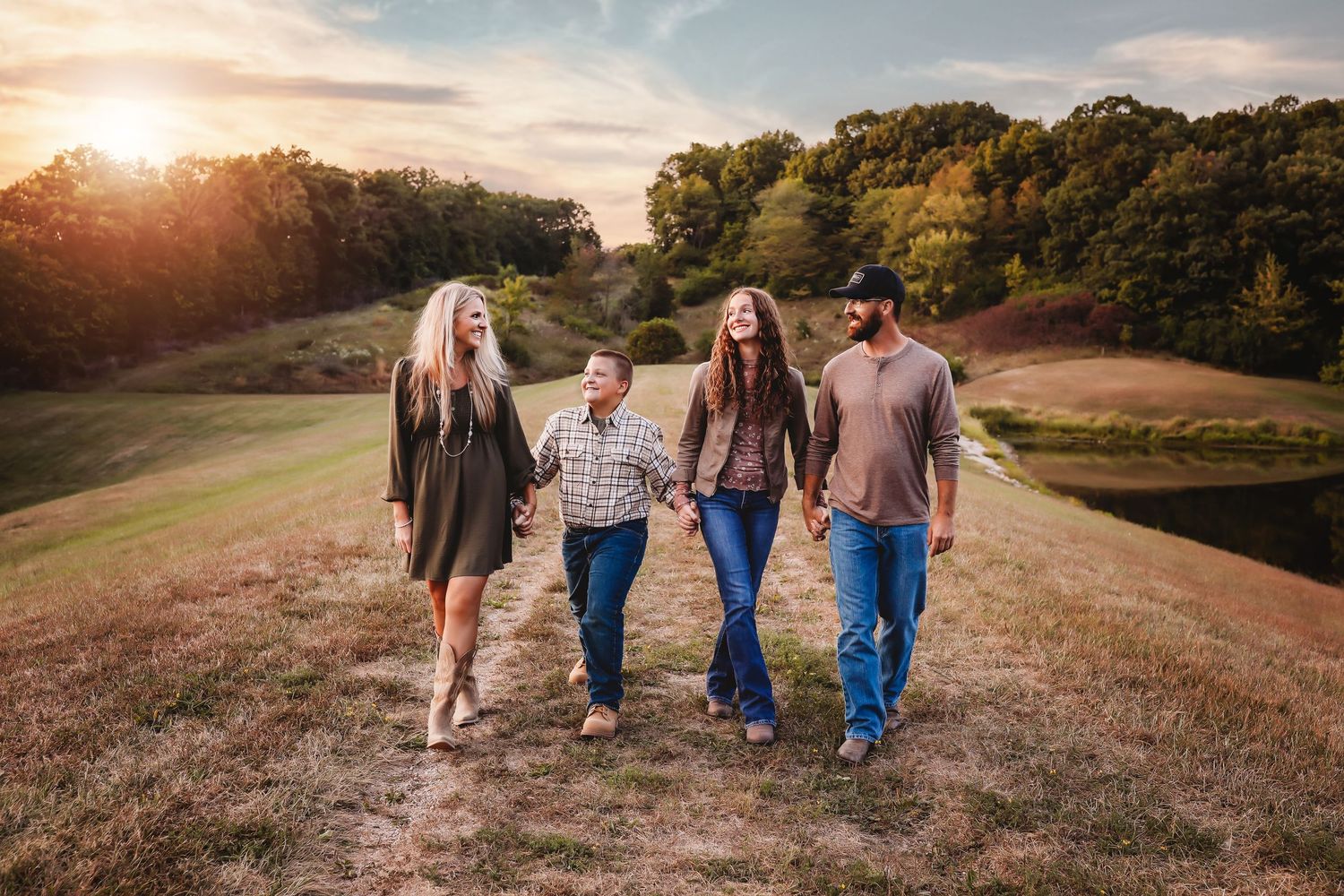 Family walking together at sunset on a grassy hill with golden sunlight in the background.