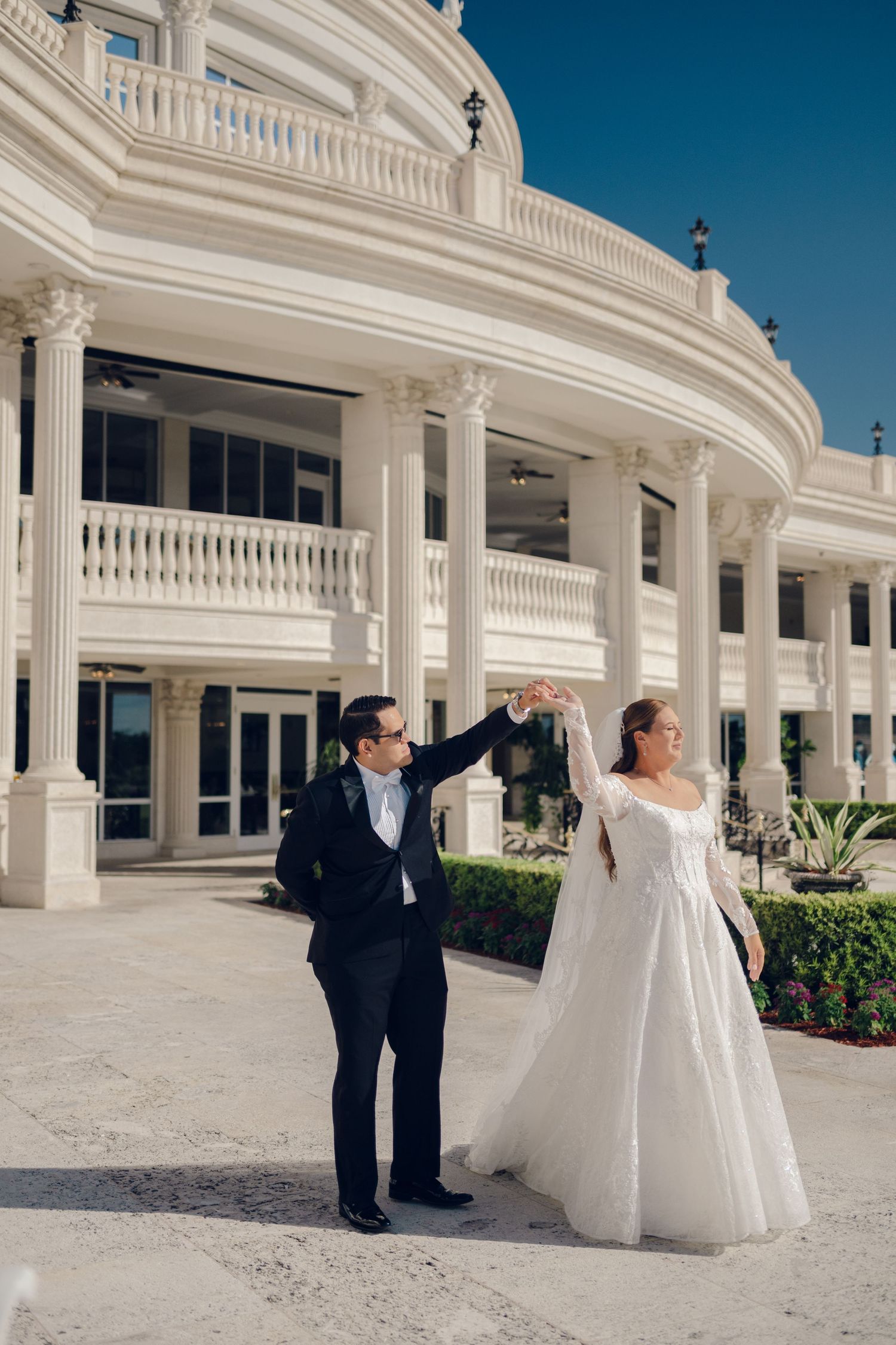 A wedding couple poses in front of a grand white columned building with elegant architecture.