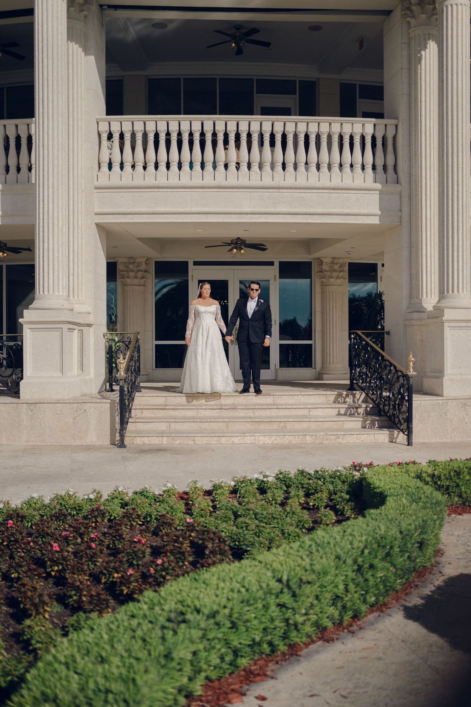 Elegant white mansion with grand columns and manicured garden beds featuring red and green landscaping.