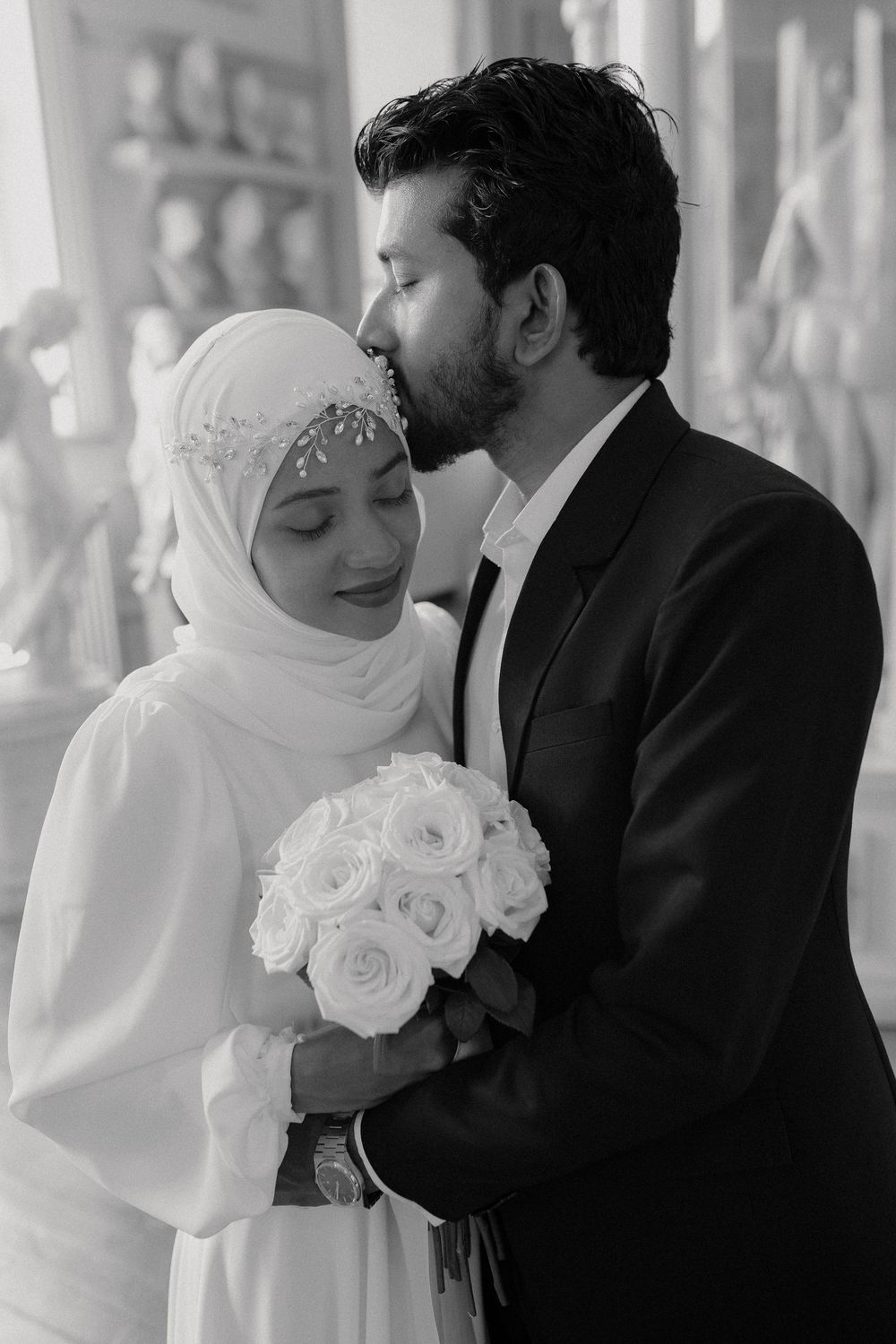 A romantic wedding moment captured in soft lighting with white roses and elegant attire.