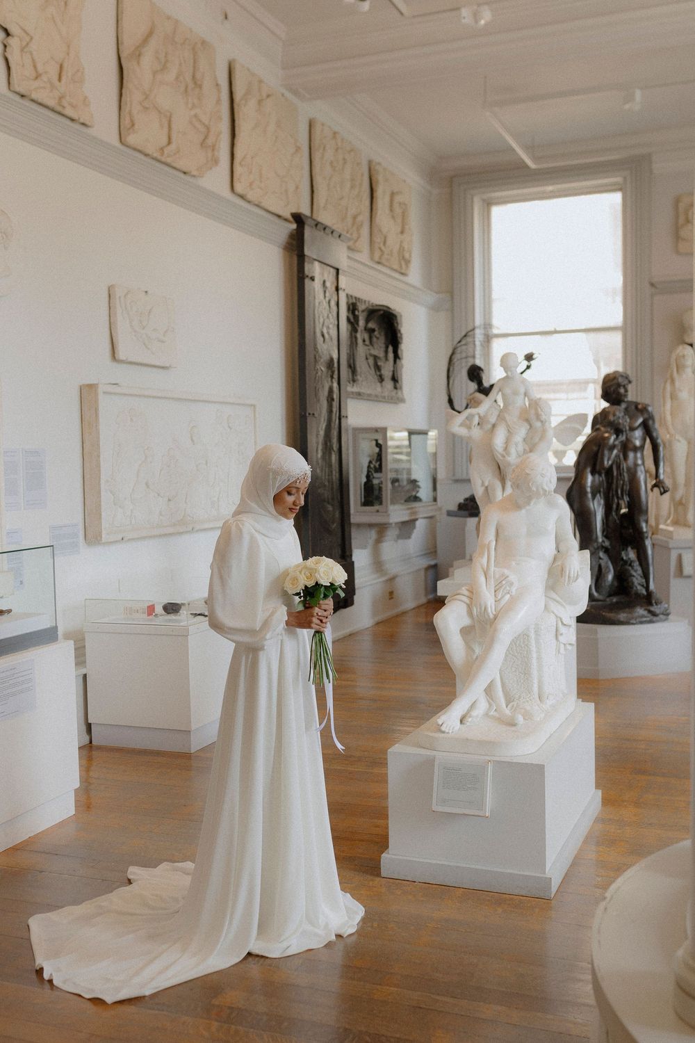 Museum gallery space with white sculptures and artwork displayed on wooden floors with natural lighting.