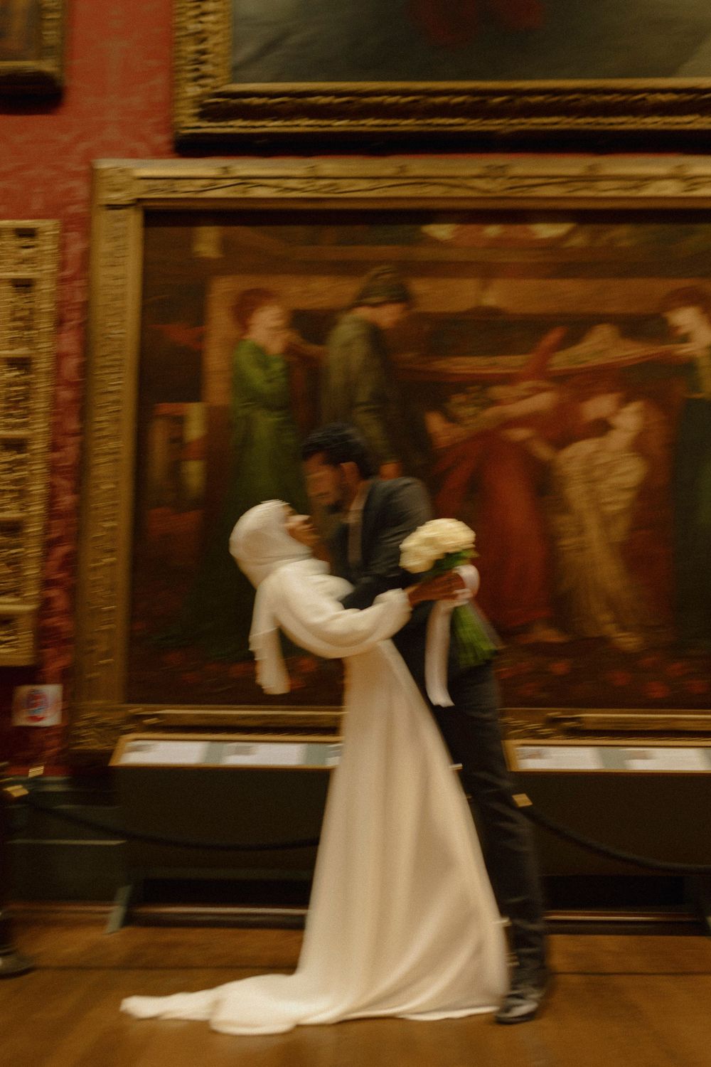 A couple dancing together in formal attire against a backdrop of classical paintings in a museum gallery.