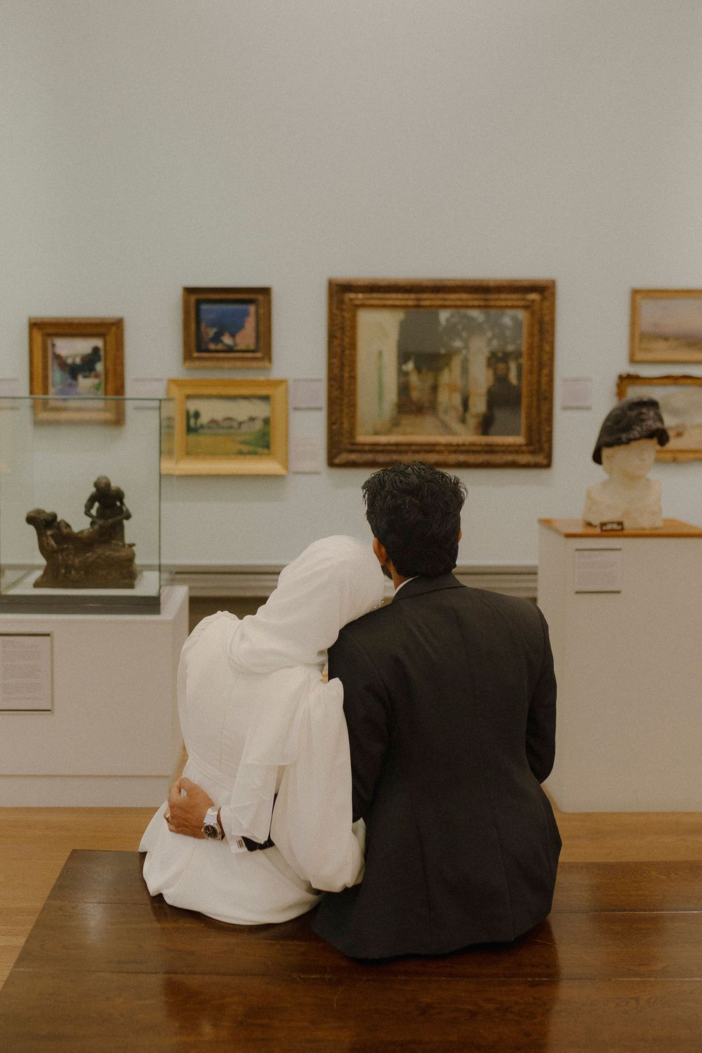 Two people in contrasting black and white outfits sit together viewing artwork in a museum gallery.