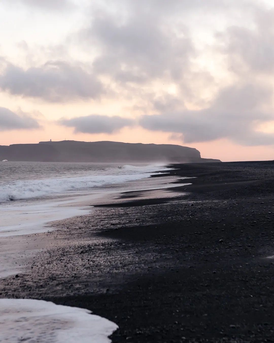 Soft sunset light over waves rolling onto a black sand beach.