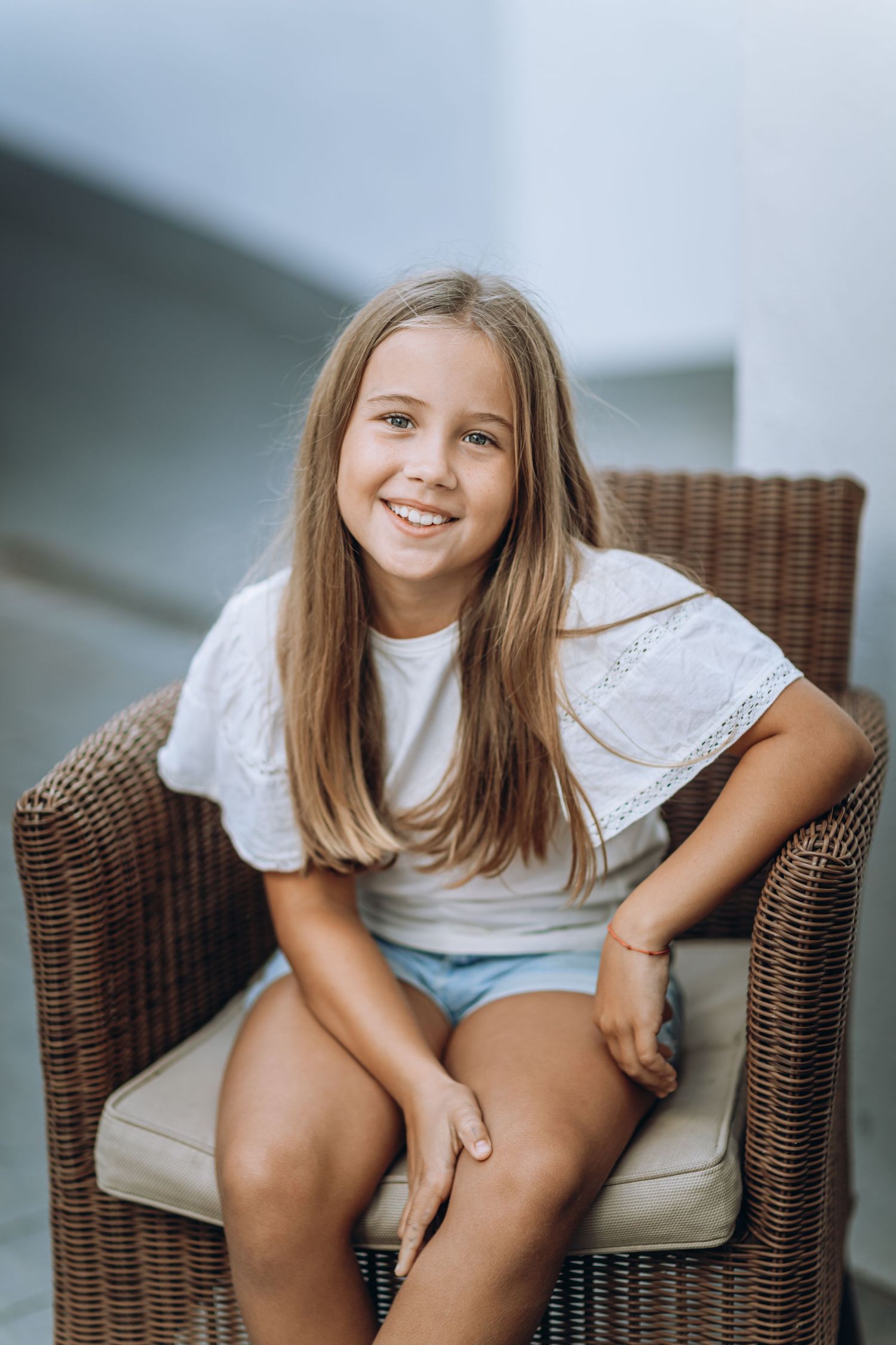 Young person relaxing in wicker chair wearing white eyelet top.