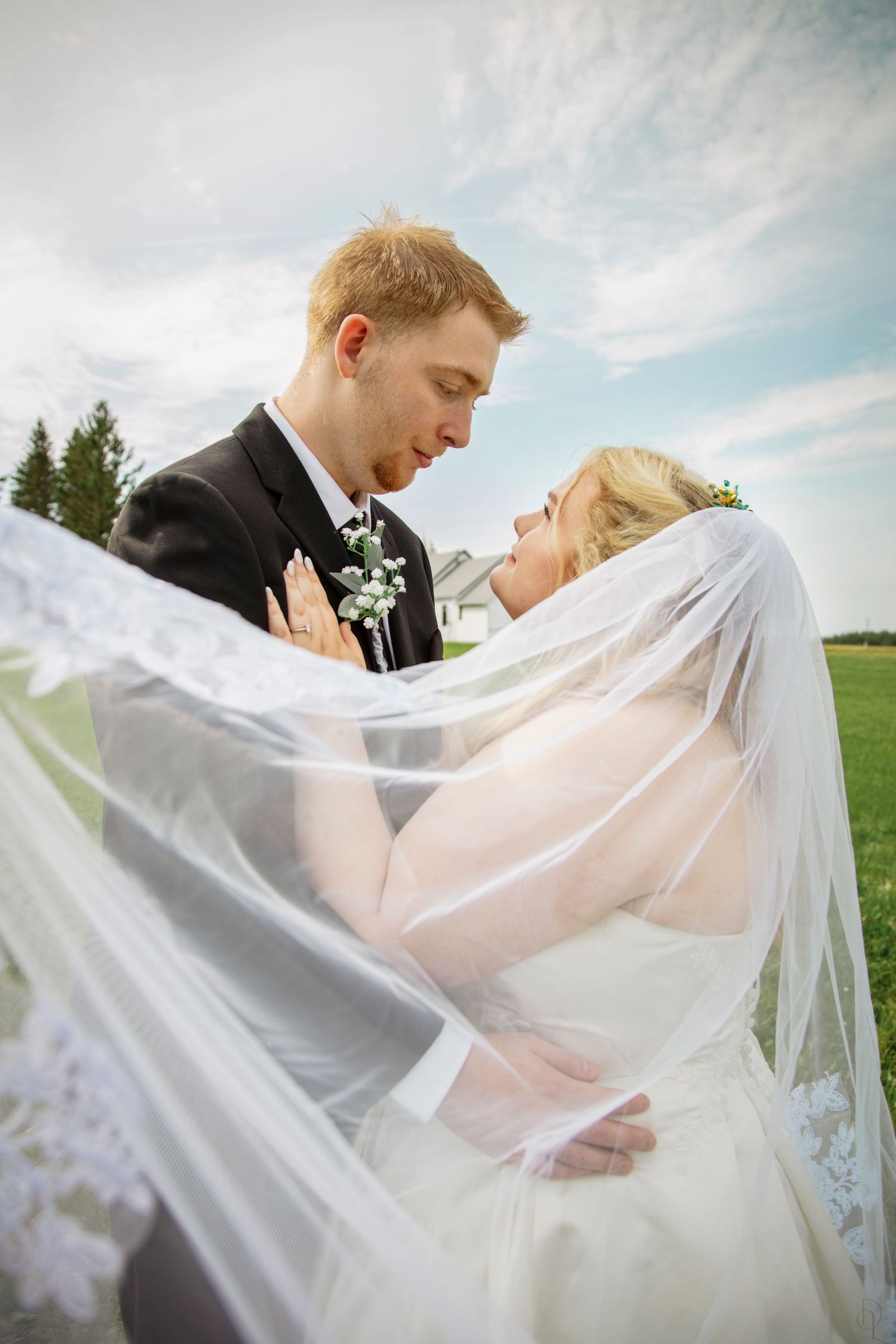 Bride and groom share a romantic moment under flowing white veil outdoors on their wedding day.