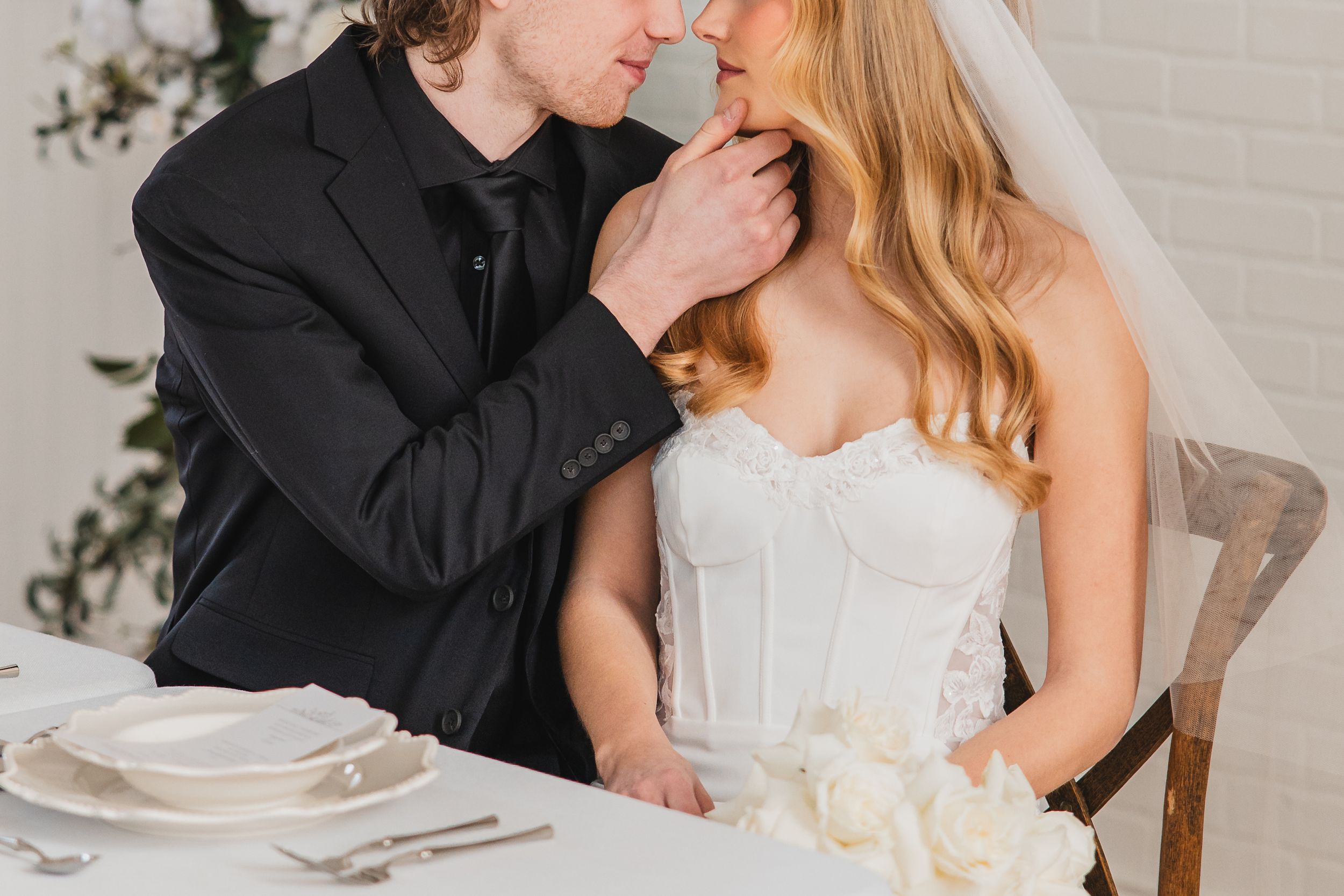 A romantic wedding couple shares an intimate moment in a white decorated setting.