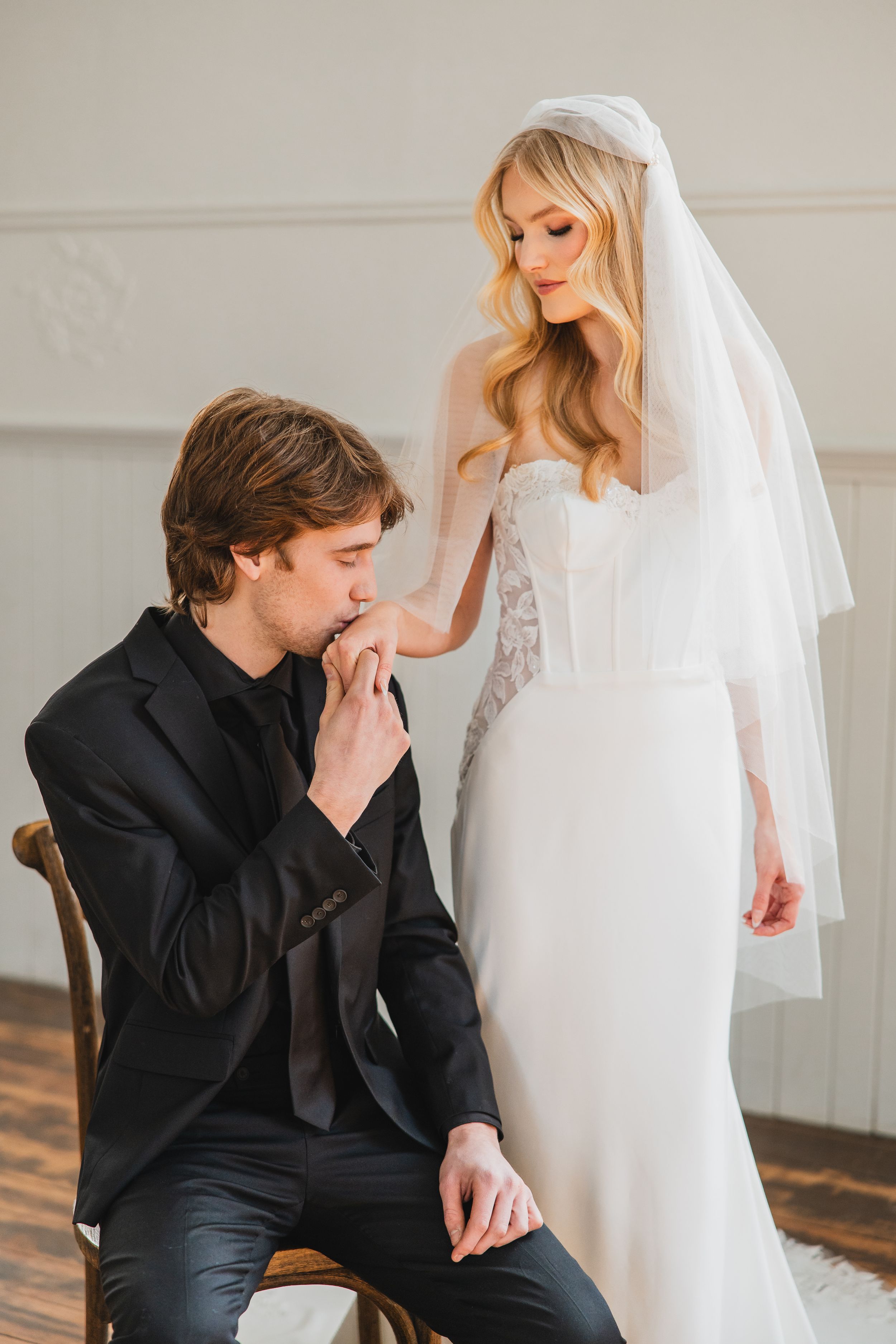 A romantic wedding moment with a bride in a fitted white gown and veil as her partner kisses her hand.