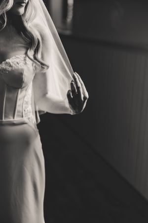 A black and white fashion photograph shows a close up of a bride in a flowing white dress standing in dramatic lighting.