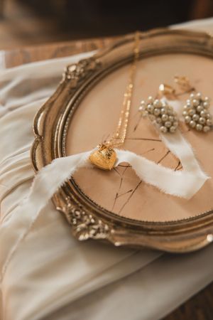 Vintage gold ornate mirror frame and delicate jewelry pieces arranged on soft white fabric in a romantic style to show wedding details.