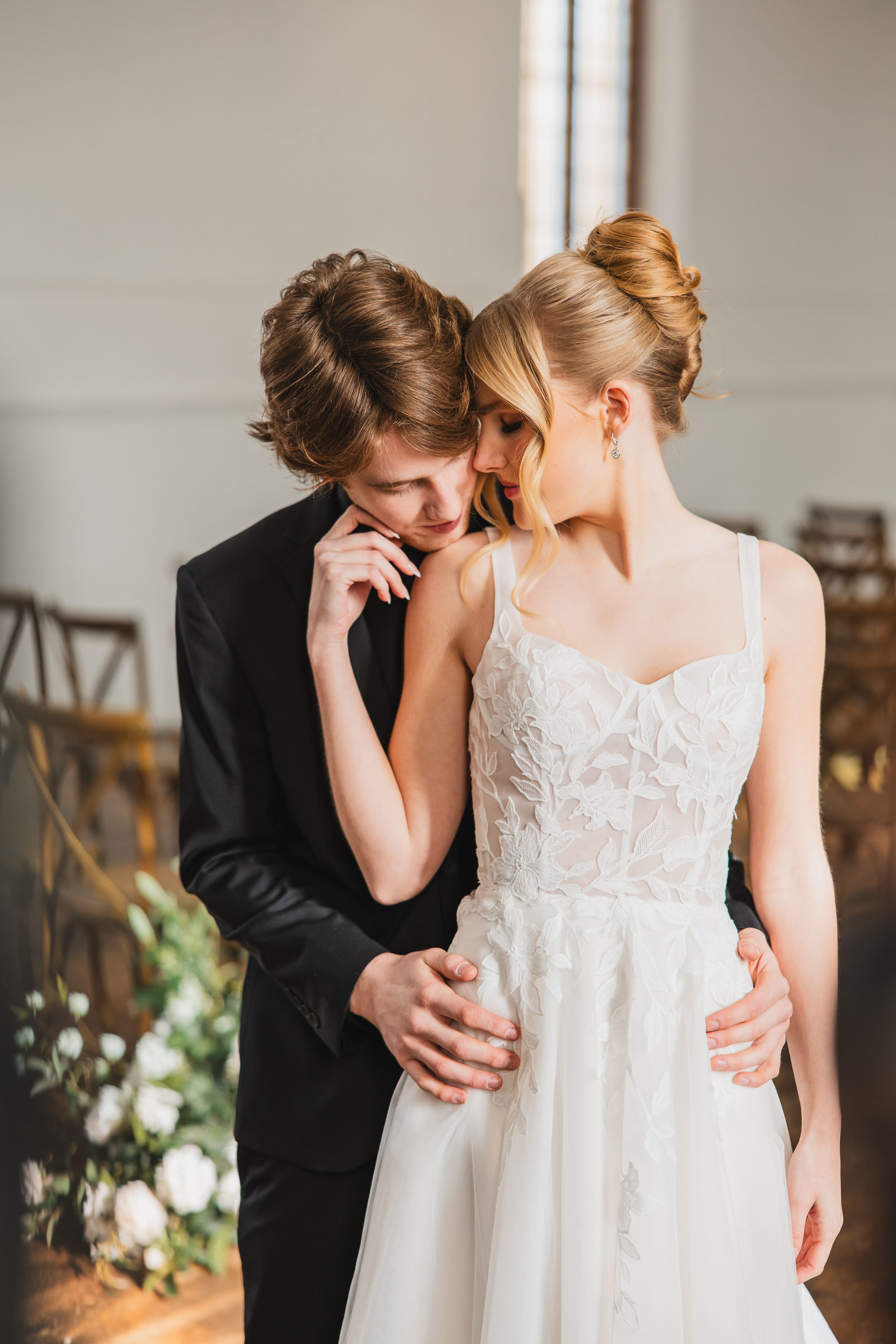 A romantic moment captured between a couple in wedding attire, with the bride in a white lace dress and groom in black suit.