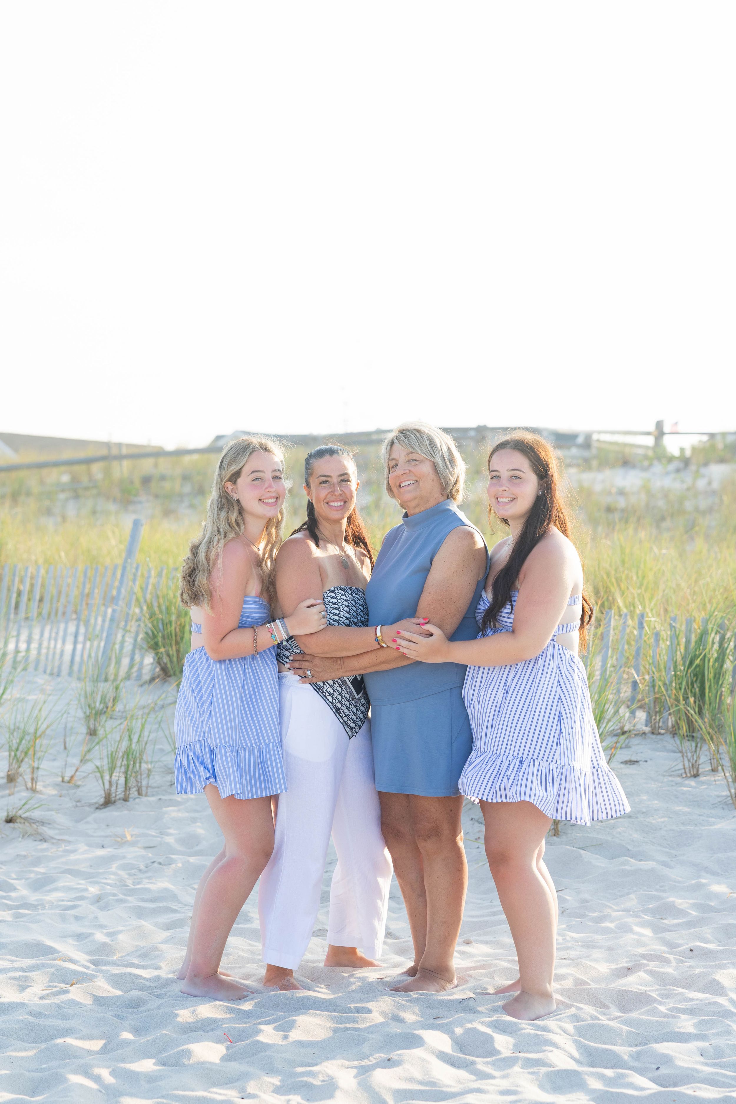 A group stands together smiling on a sandy beach with sand dunes and sea grass in the background on a sunny day.