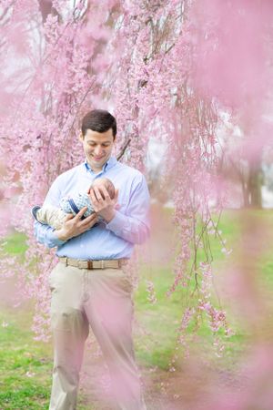 A tender moment captured under blooming cherry blossoms with a newborn baby.