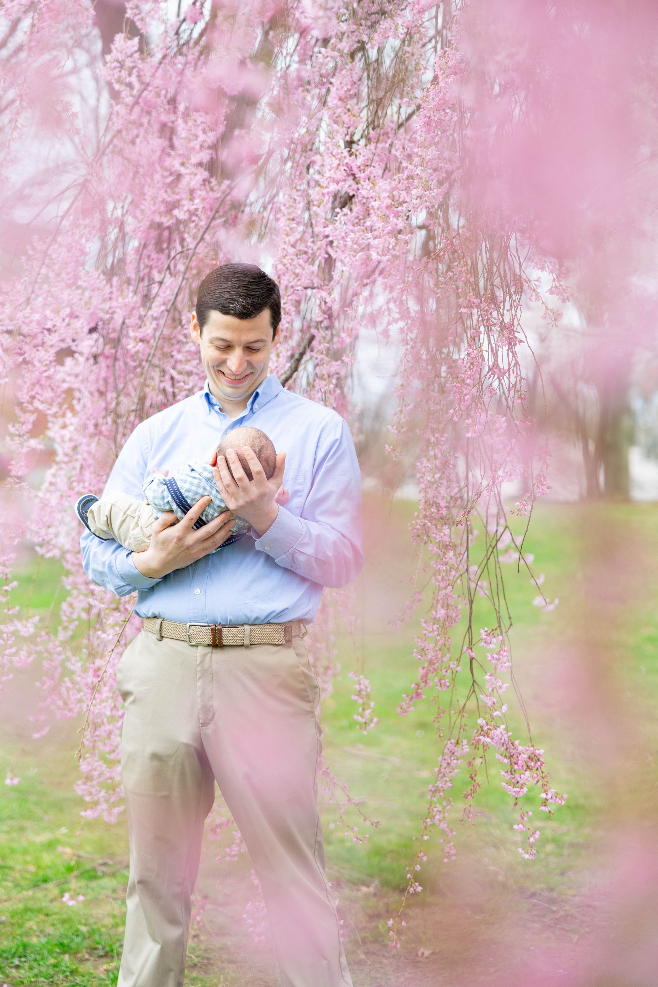 A tender moment captured under blooming cherry blossoms with a newborn baby.