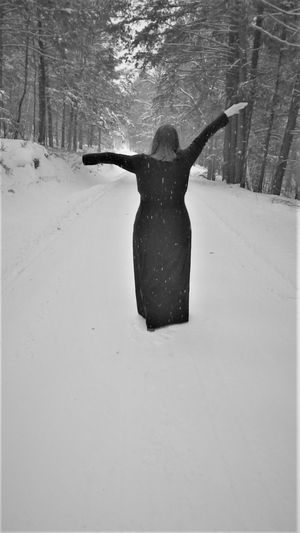 A person in dark clothing stands in deep snow surrounded by tall evergreen trees in winter.