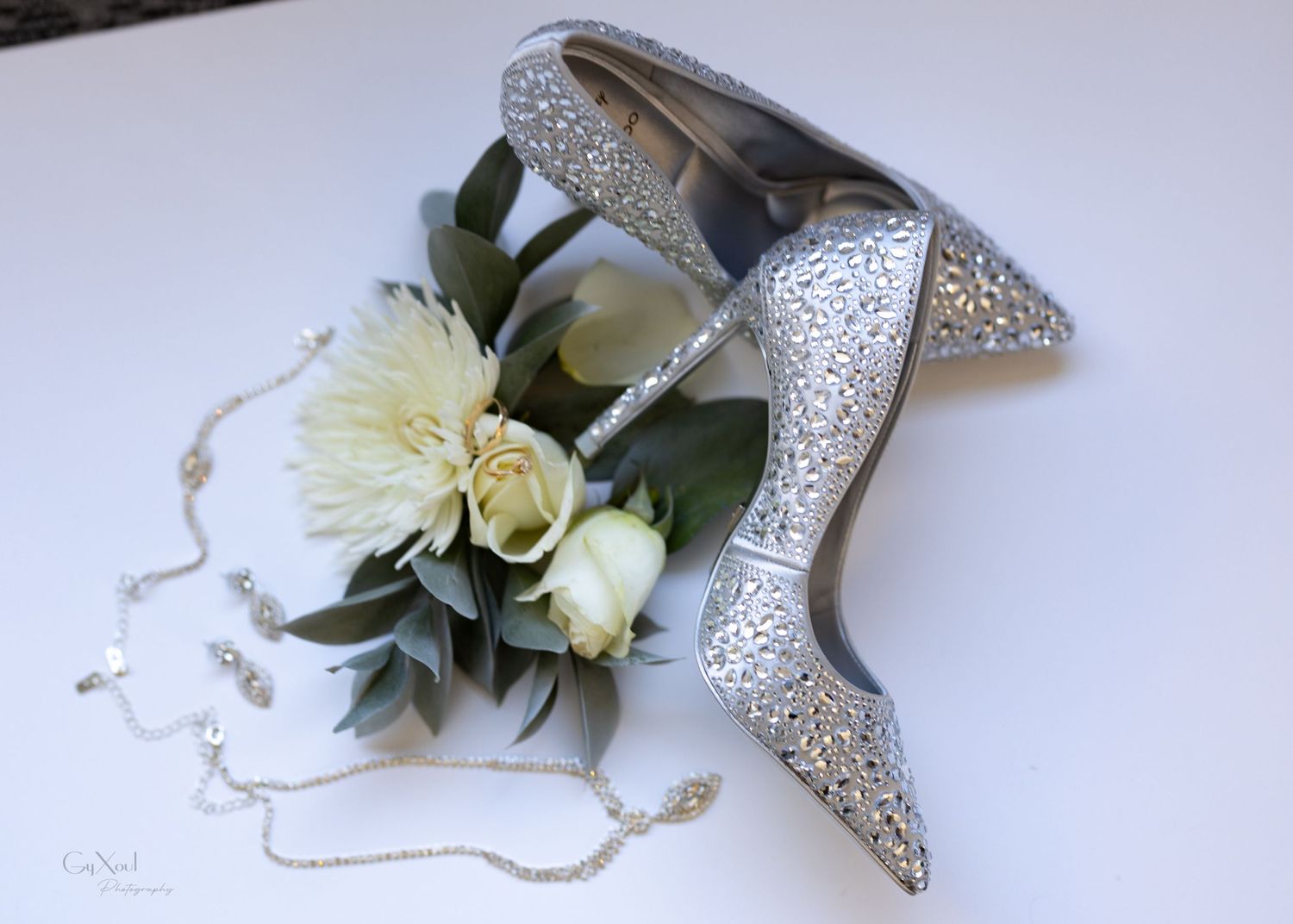 Glittery silver wedding heels with white floral arrangement and delicate jewelry.