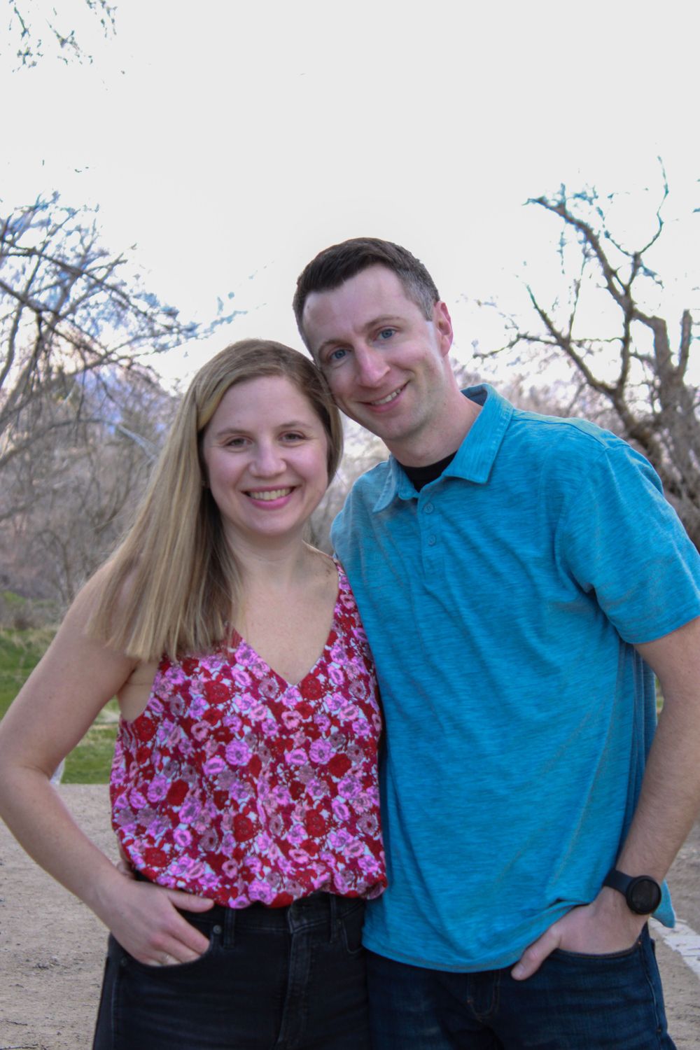 A couple in coordinating blue and pink outfits smiles together on a nature path.