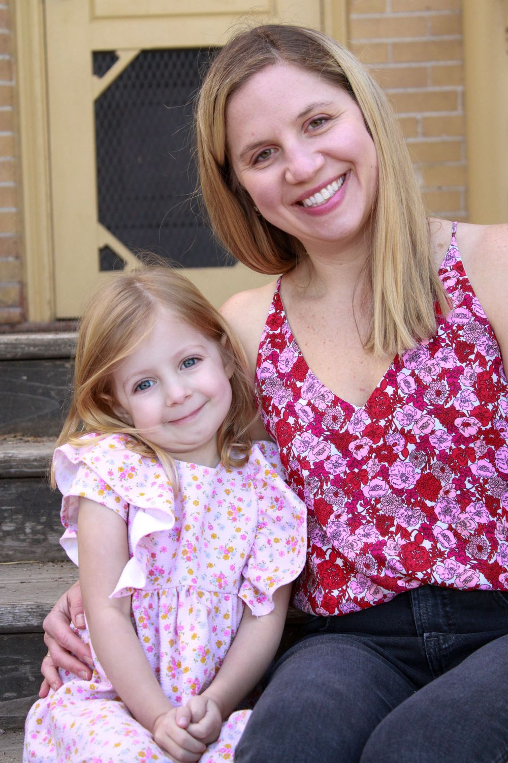 A parent and child in matching floral patterns sit together on outdoor steps.