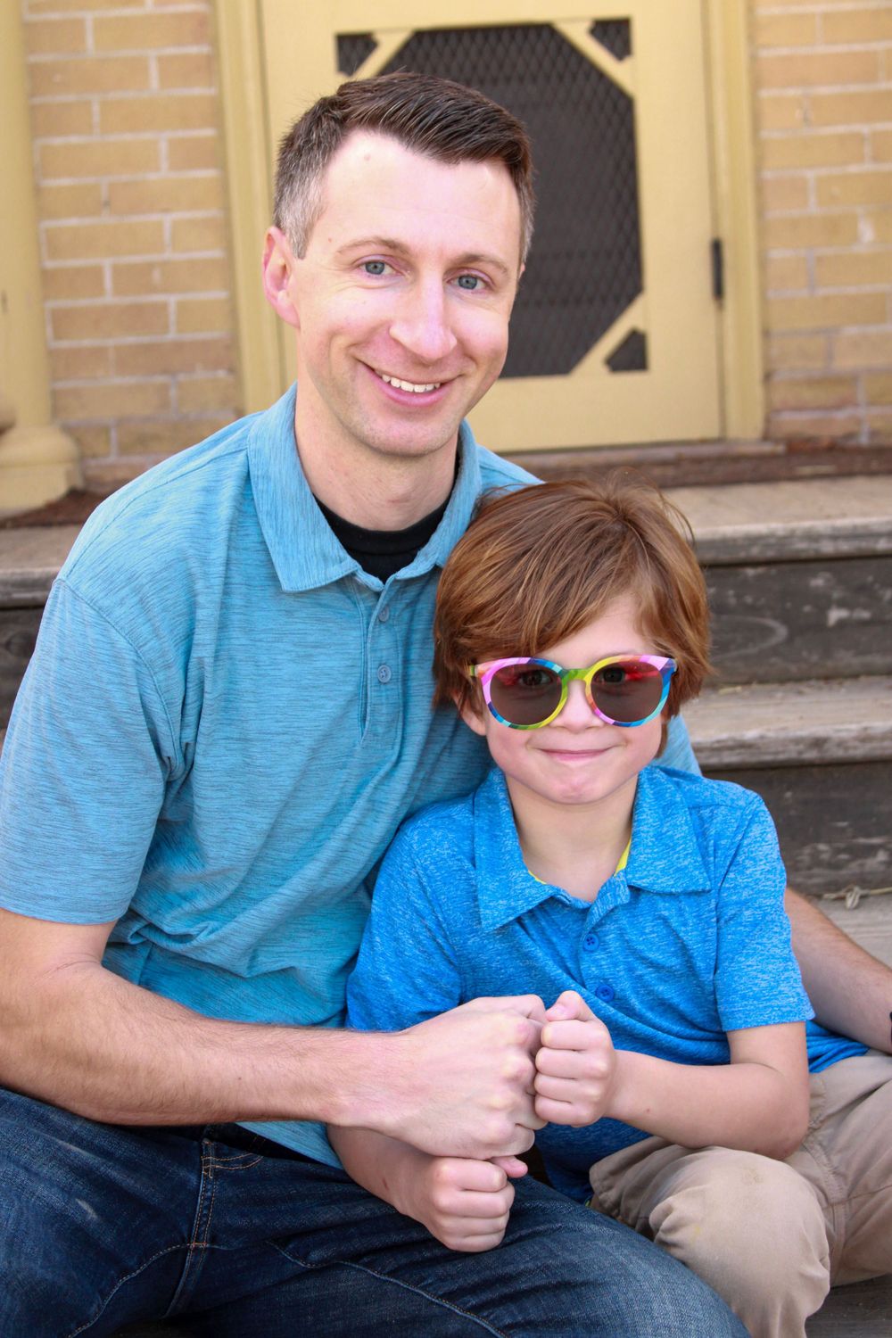 A cheerful pair in matching blue shirts pose together on outdoor steps.