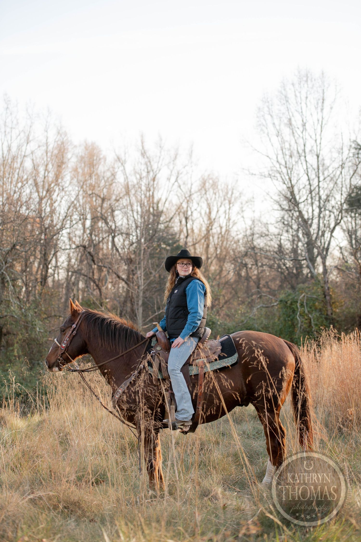 Western rider on brown horse standing in field of dried grass during winter.