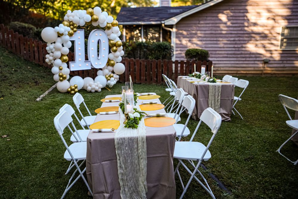 Elegant outdoor table setting with white chairs and balloon arch displaying number 10.