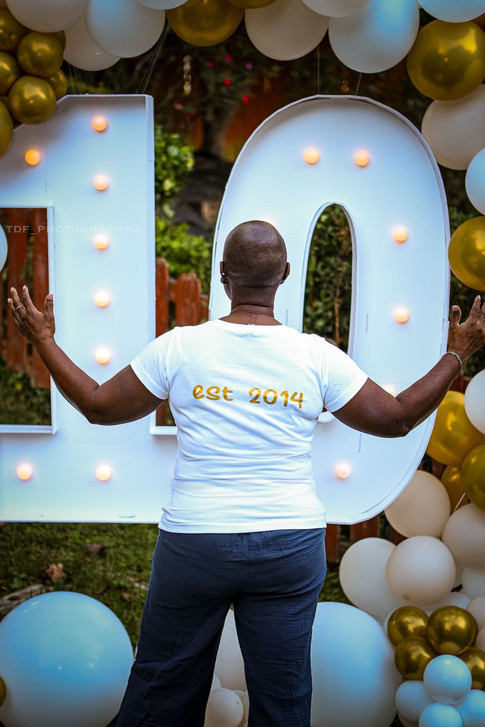 Person in white t-shirt standing in front of large light-up number 10 with balloon decorations.