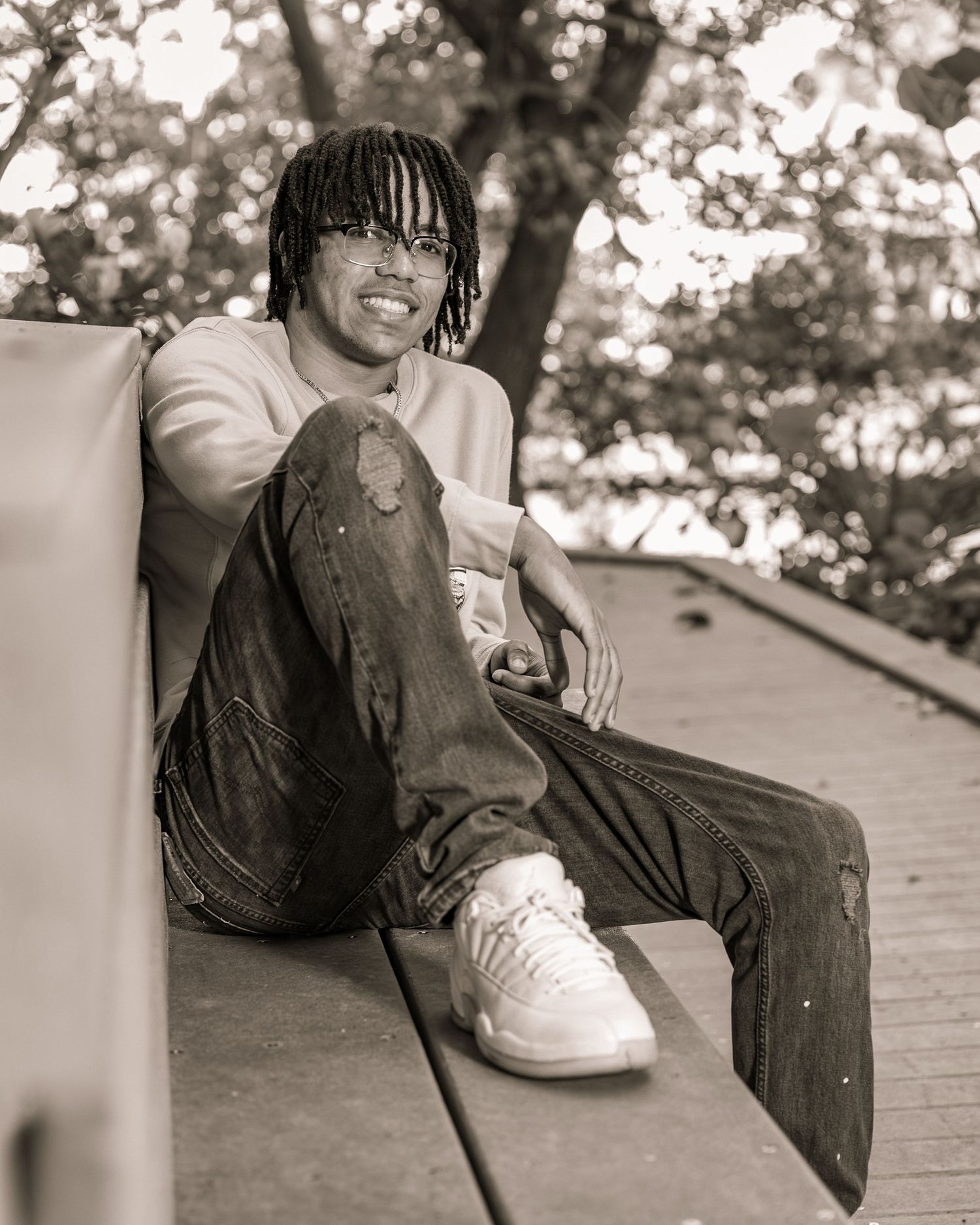 A sepia-toned portrait of someone in casual wear and white sneakers sitting on a bench outdoors with a relaxed pose.