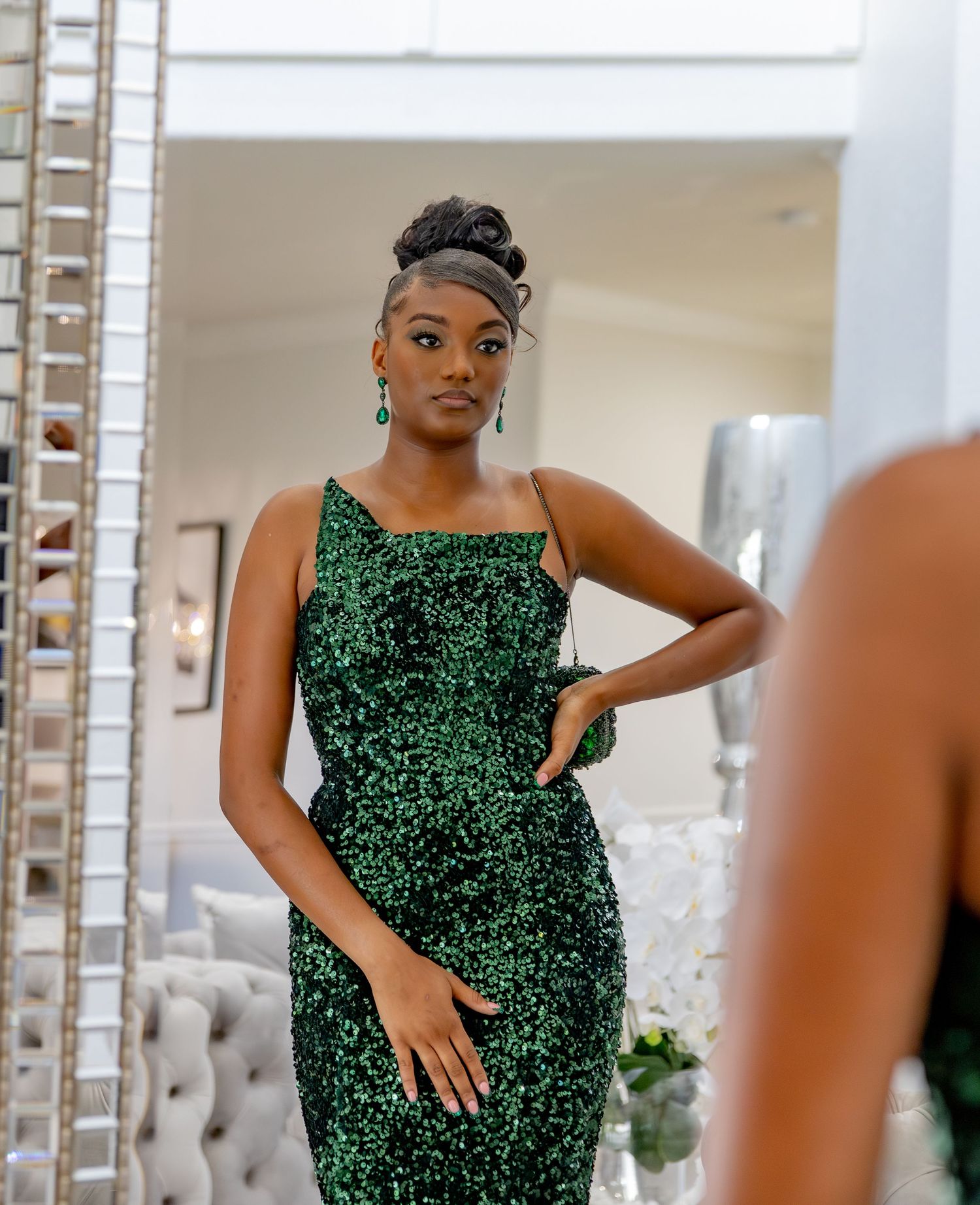 Someone poses in a sparkly emerald green evening gown with a fitted silhouette in an elegant room with mirrors.