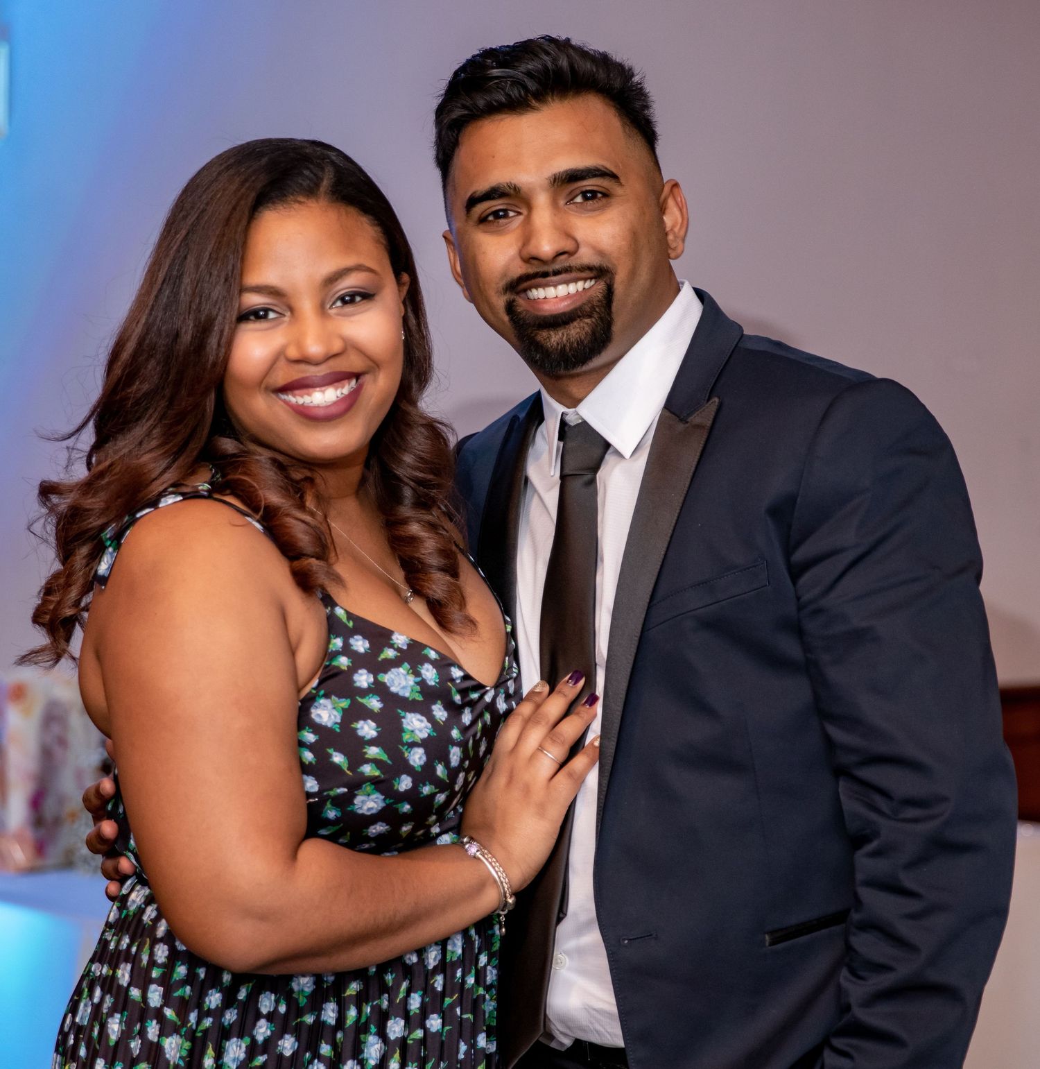 A couple in formal attire pose together at a special event with blue lighting in the background.