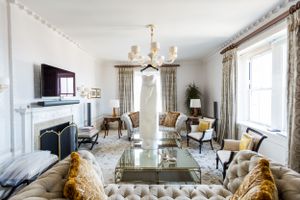 Luxurious living room with tufted couch, glass coffee table, chandelier and floral curtains in soft neutral colors.
