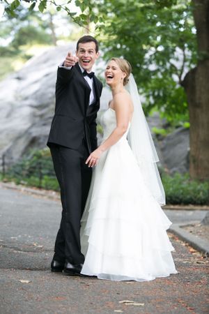 A joyful bride and groom share a candid moment together on their wedding day in a park with greenery.